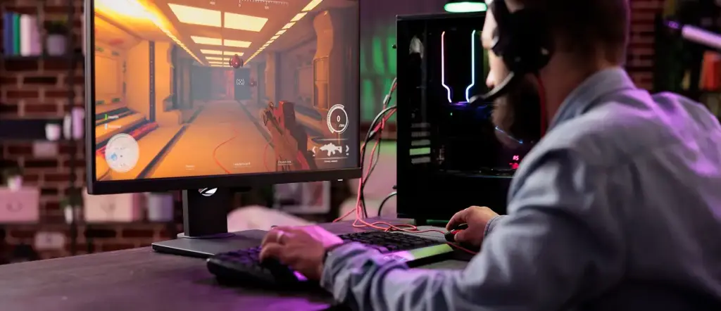 Een jongen zit in een lichte kamer achter een computer te gamen.