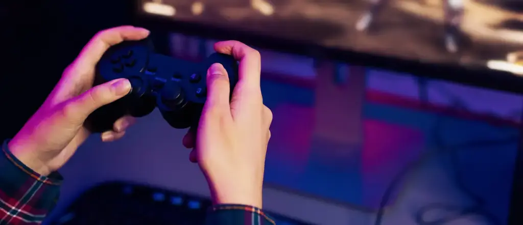 Een jongen met een gamepad in zijn handen zit voor een monitor en speelt een spel.